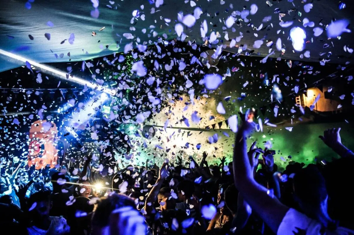 Escena dinámica de discoteca con luces vibrantes y confeti cayendo sobre una multitud de bailarines (imagen de referencia)