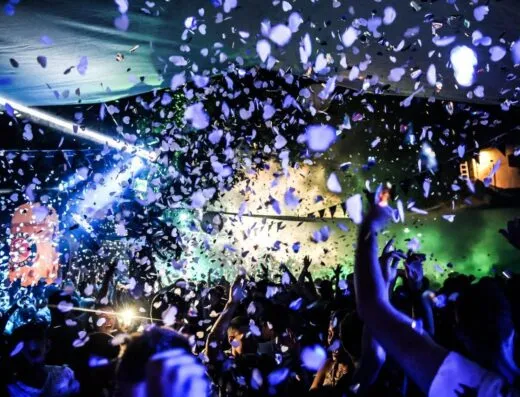 Escena dinámica de discoteca con luces vibrantes y confeti cayendo sobre una multitud de bailarines.