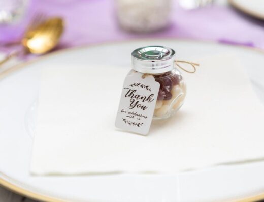 Primer plano de un pequeño tarro de vidrio con una etiqueta de agradecimiento colocado en un plato, perfecto para bodas o eventos.