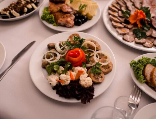 Platos gourmet bellamente dispuestos con carnes, quesos y guarniciones en una mesa blanca.