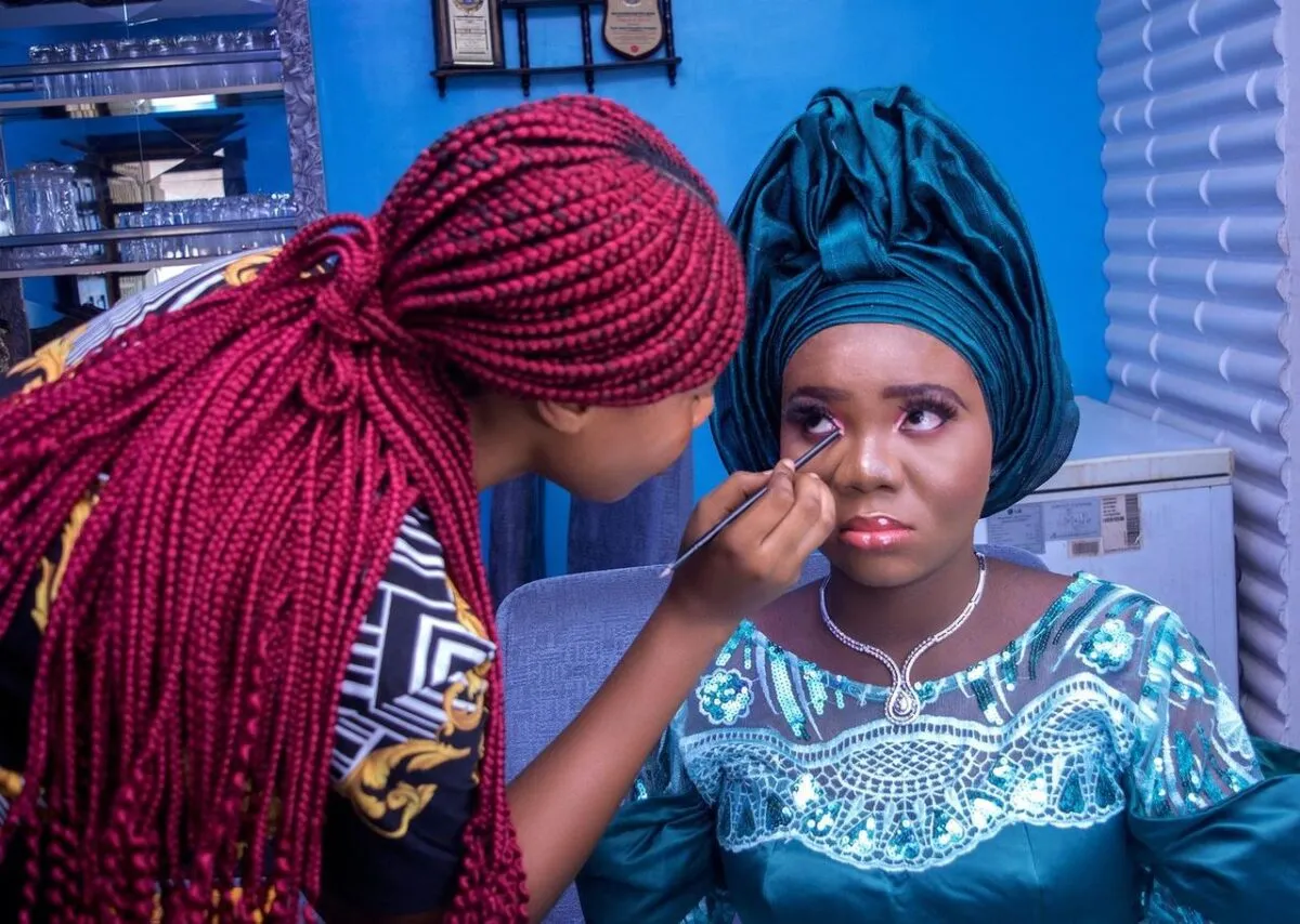 Una mujer nigeriana vestida con traje tradicional recibiendo maquillaje de un artista de maquillaje en interiores (imagen de referencia)