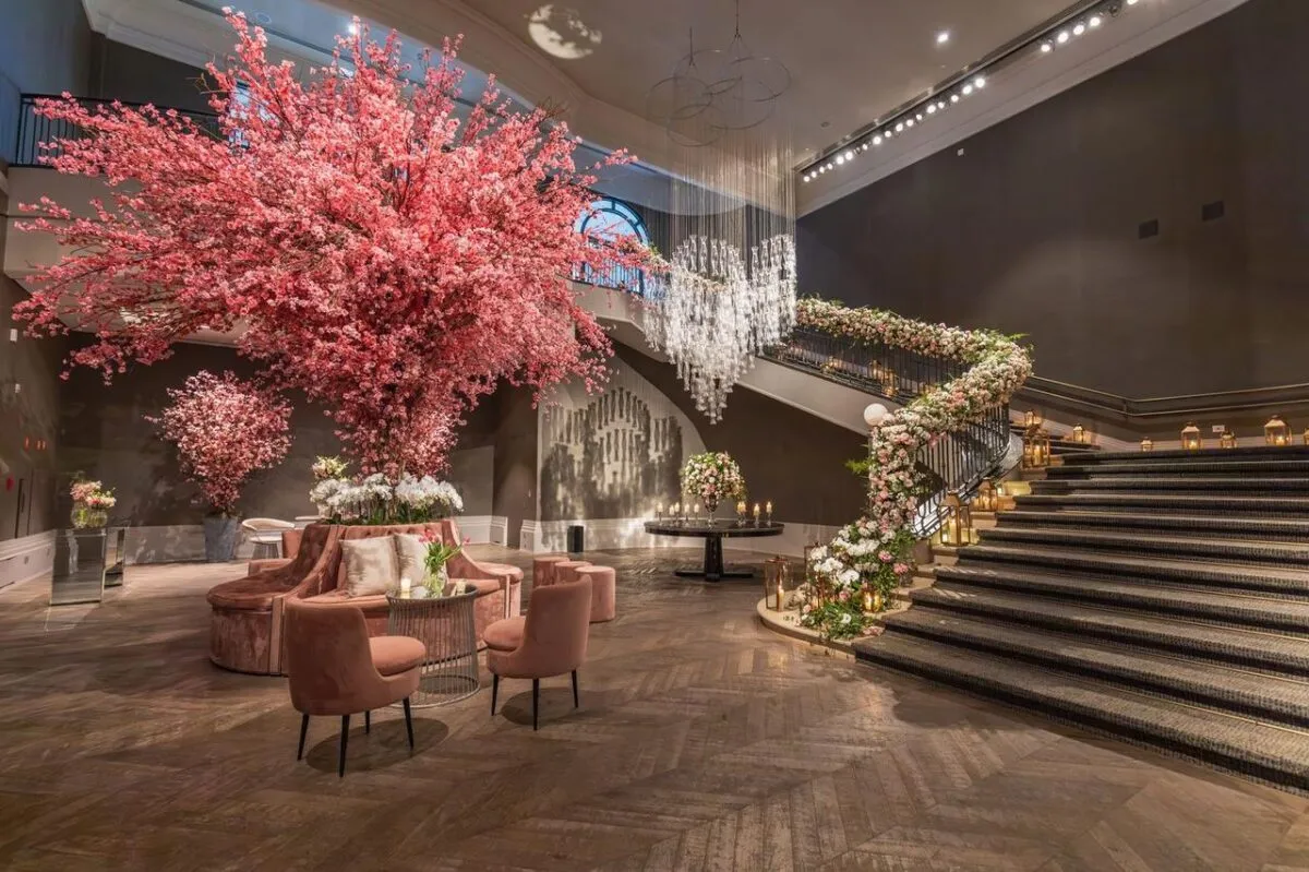 Lobby de hotel lujoso con grandes arreglos florales y escalera elegante (imagen de referencia)