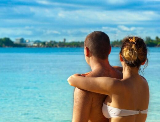 Una pareja abrazándose y disfrutando de la vista en una playa tropical soleada, simbolizando amor y relajación.
