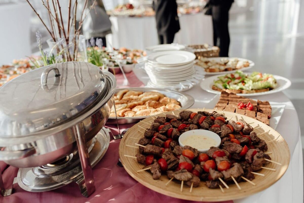 Elegante buffet con carnes en brochetas, ensaladas frescas y postres variados en un evento festivo (imagen de referencia)