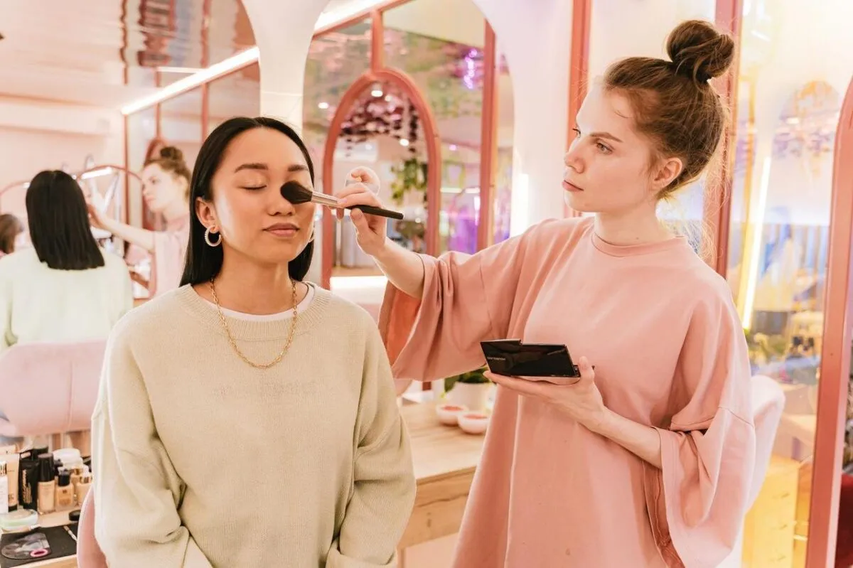 Mujer asiática recibiendo maquillaje de un artista en un salón de belleza moderno y luminoso (imagen de referencia)