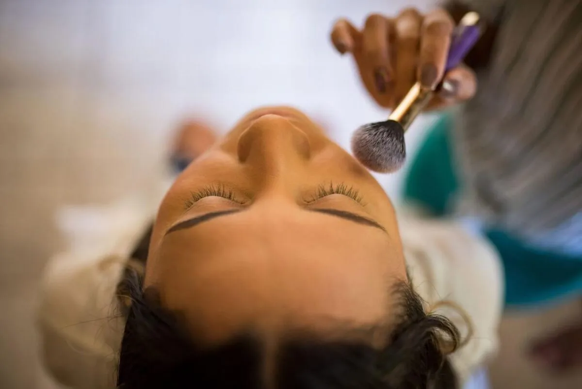 Vista en primer plano de un maquillador aplicando rubor con un pincel en el rostro de una mujer (imagen de referencia)