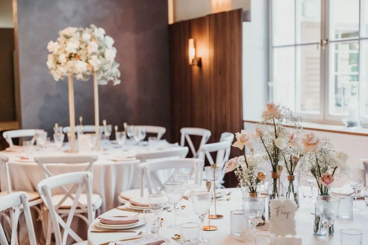 Montaje de boda lujoso con manteles blancos, centros de flores y vajilla elegante en un lugar brillante (imagen de referencia)