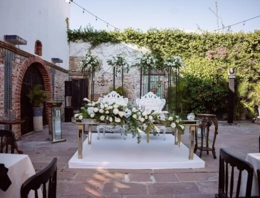 Hermosa organización de boda con elegantes arreglos florales y asientos en un patio al aire libre.