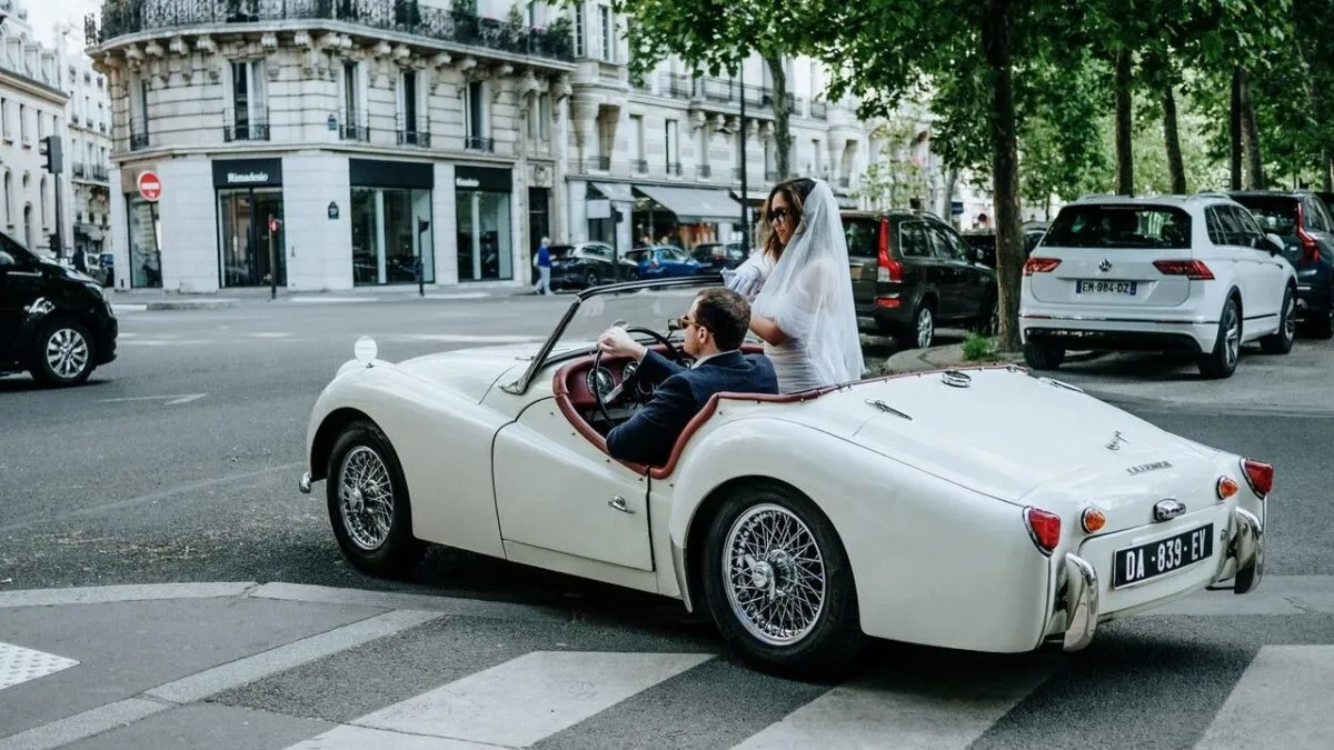 Novia y novio en un coche convertible blanco clásico en una calle de París, celebrando su día de boda (imagen de referencia)