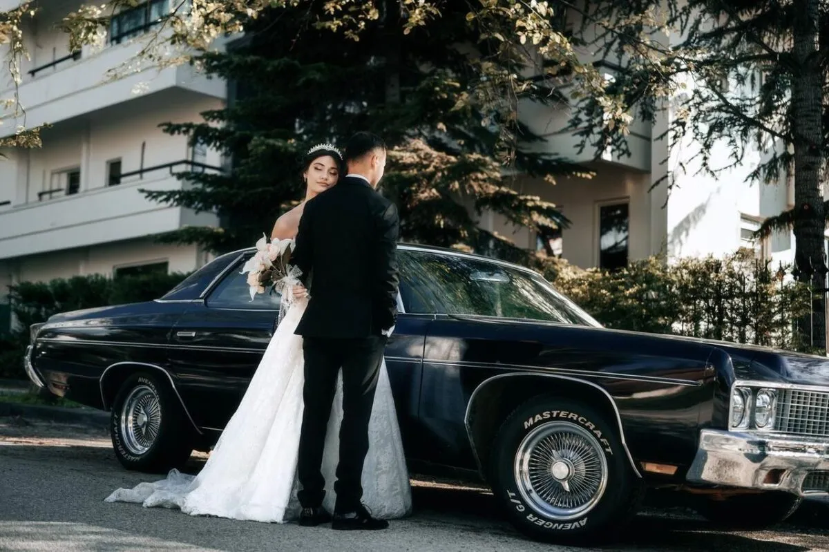 Una novia y un novio posan junto a un coche clásico al aire libre el día de su boda (imagen de referencia)
