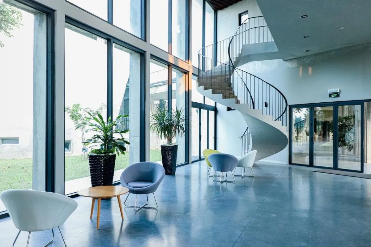 Lobby espacioso con escalera en espiral, grandes ventanas y zona de estar moderna (imagen de referencia)