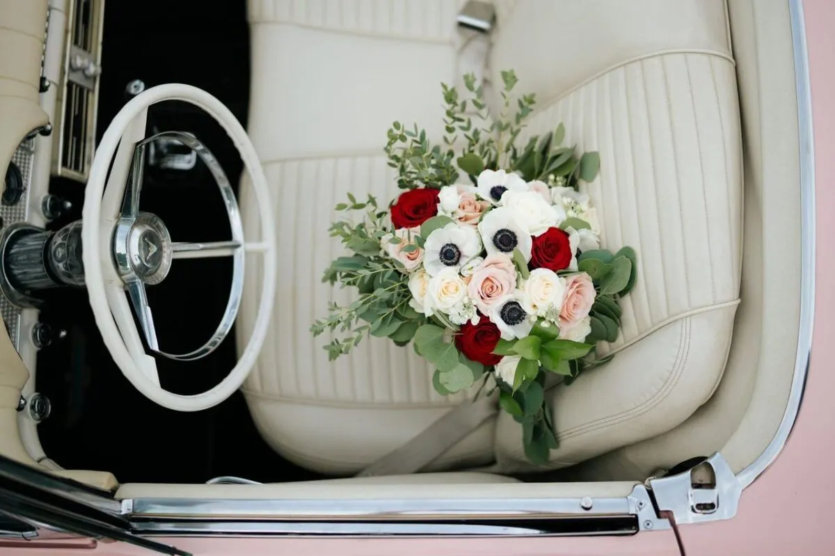 Un precioso arreglo floral con rosas y anémonas colocado en el interior del asiento de cuero blanco de un coche clásico (imagen de referencia)