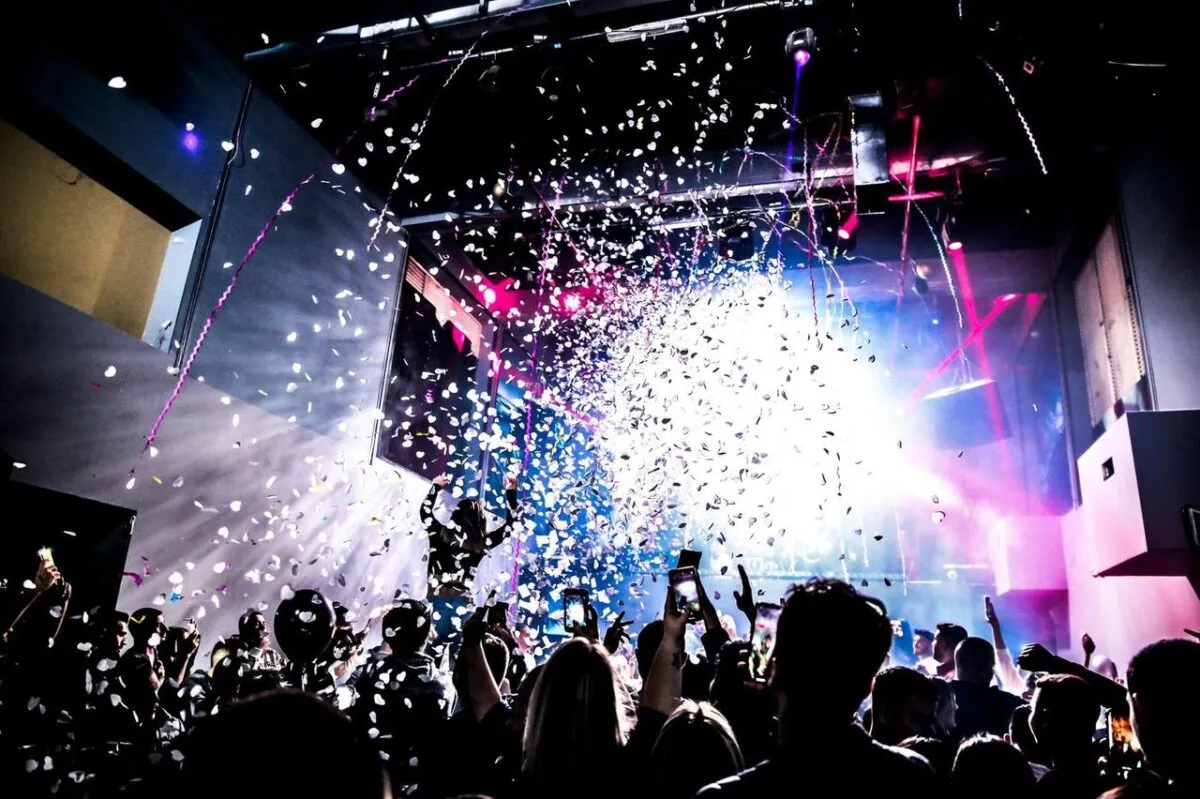Escena energética de discoteca con una multitud bailando bajo confeti y luces coloridas (imagen de referencia)