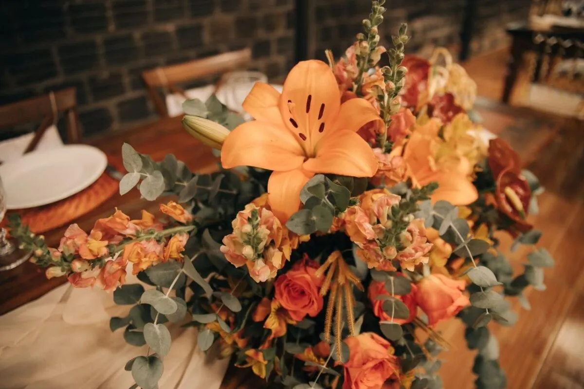 Hermoso arreglo floral con lirios naranjas y rosas, perfecto para la decoración de banquetes o eventos (imagen de referencia)