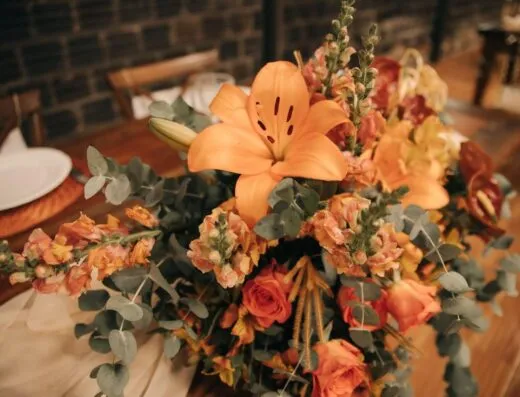 Hermoso arreglo floral con lirios naranjas y rosas, perfecto para la decoración de banquetes o eventos.