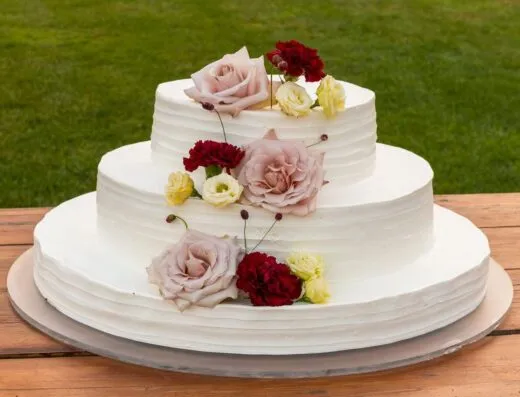 Una tarta de boda bellamente decorada de tres niveles adornada con elegantes rosas al aire libre.