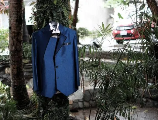 Un traje azul elegante cuelga en un árbol al aire libre, rodeado de exuberante vegetación.