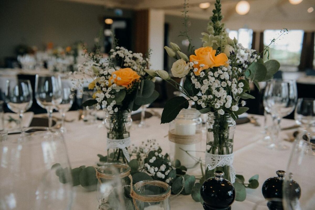 Configuración de mesa elegante en restaurante con centros de mesa florales y cristalería, perfecta para bodas o eventos (imagen de referencia)