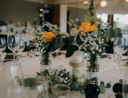 Configuración de mesa elegante en restaurante con centros de mesa florales y cristalería, perfecta para bodas o eventos.